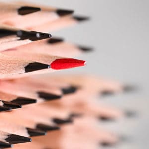 Featured image of blogpost "10 Career Tips for Women in Male-Dominated Industries" showing a one red pencil among simple pencils on a gray background