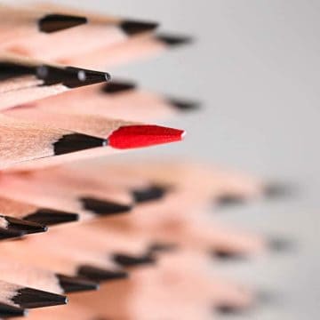 Featured image of blogpost "10 Career Tips for Women in Male-Dominated Industries" showing a one red pencil among simple pencils on a gray background